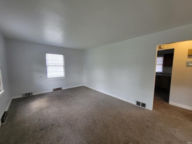 spare room featuring visible vents, baseboards, and dark carpet