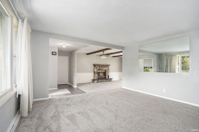 unfurnished living room featuring ceiling fan, beamed ceiling, carpet, a stone fireplace, and a baseboard heating unit