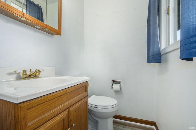 half bath featuring baseboards, vanity, toilet, and wood finished floors