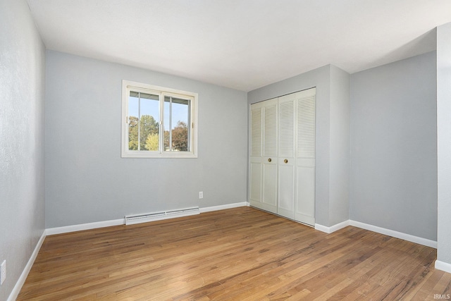 unfurnished bedroom with baseboards, a closet, a baseboard radiator, and light wood-style floors