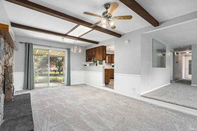 unfurnished living room with light carpet, a wainscoted wall, beam ceiling, and ceiling fan with notable chandelier