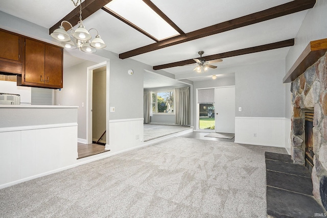 unfurnished living room with carpet floors, a fireplace, wainscoting, beamed ceiling, and ceiling fan with notable chandelier