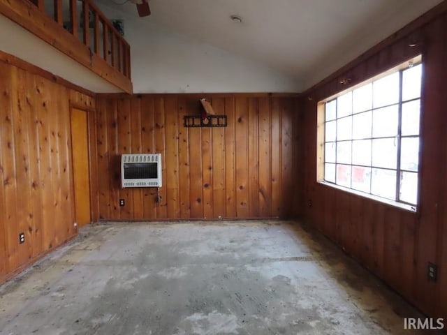 empty room featuring lofted ceiling, wooden walls, a ceiling fan, heating unit, and unfinished concrete floors