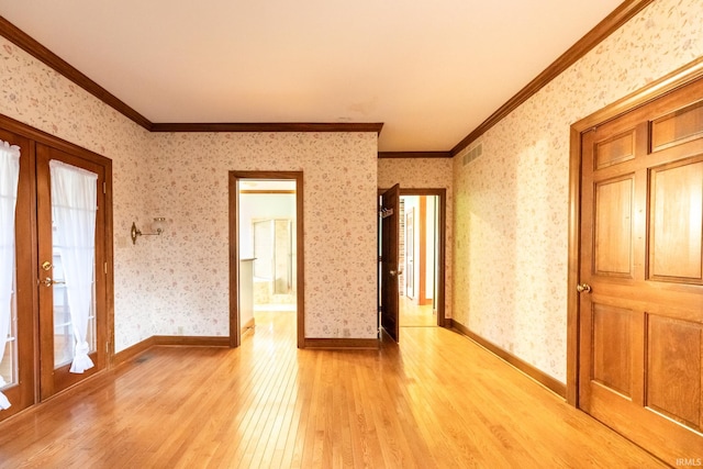 spare room featuring ornamental molding, visible vents, light wood finished floors, and wallpapered walls