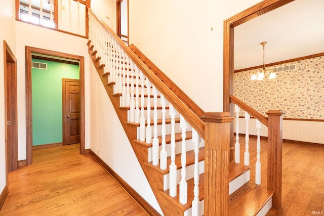 stairway with a notable chandelier, visible vents, wood finished floors, baseboards, and wallpapered walls