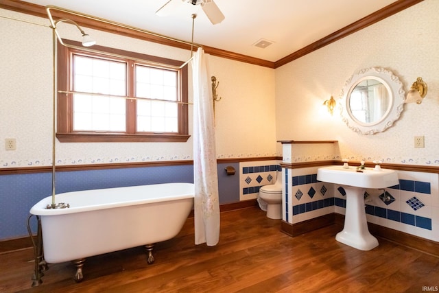 full bathroom featuring toilet, wallpapered walls, a wainscoted wall, and wood finished floors