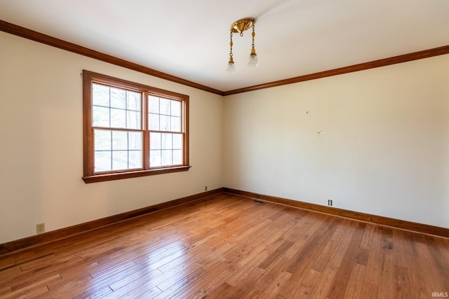 spare room with baseboards, light wood finished floors, visible vents, and crown molding