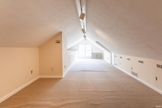 additional living space with carpet, visible vents, a textured ceiling, and baseboards