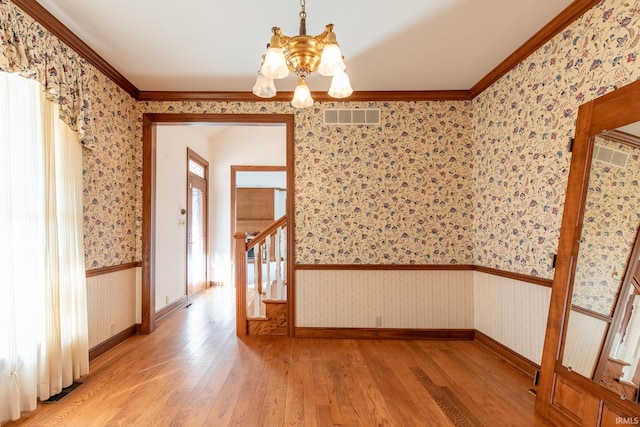 unfurnished room with a wainscoted wall, light wood-style floors, visible vents, and wallpapered walls