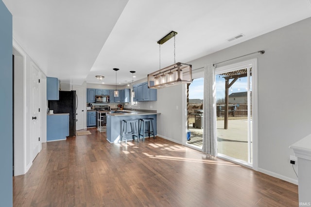 kitchen with dark wood-style floors, a peninsula, appliances with stainless steel finishes, and blue cabinetry