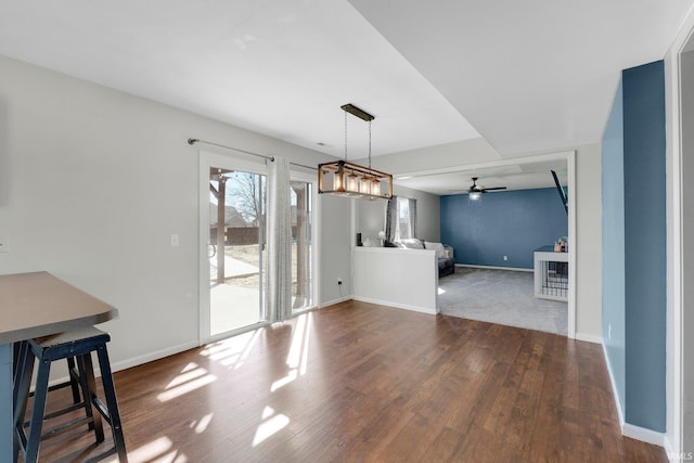 unfurnished dining area featuring dark wood-style floors, ceiling fan, and baseboards