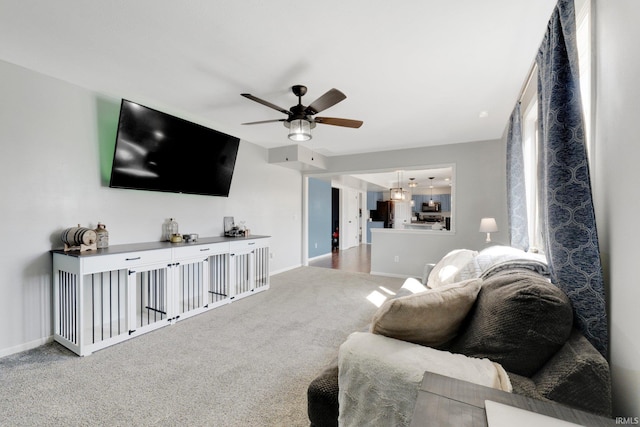 carpeted living area with ceiling fan and baseboards