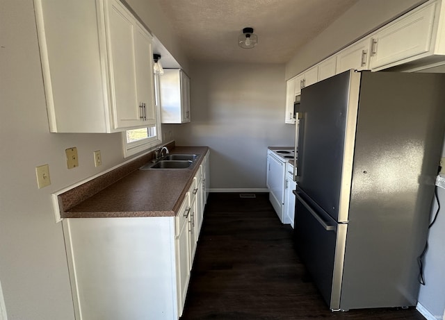 kitchen with dark countertops, freestanding refrigerator, white cabinetry, a sink, and baseboards