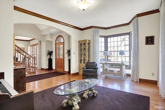 living room featuring ornamental molding, arched walkways, baseboards, and wood finished floors