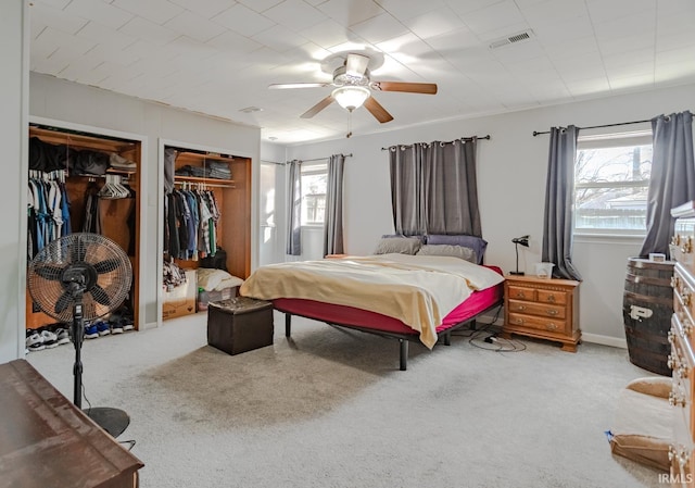 carpeted bedroom featuring multiple closets, visible vents, and ceiling fan