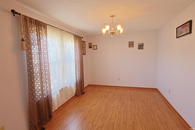 spare room with light wood-type flooring, baseboards, and a notable chandelier