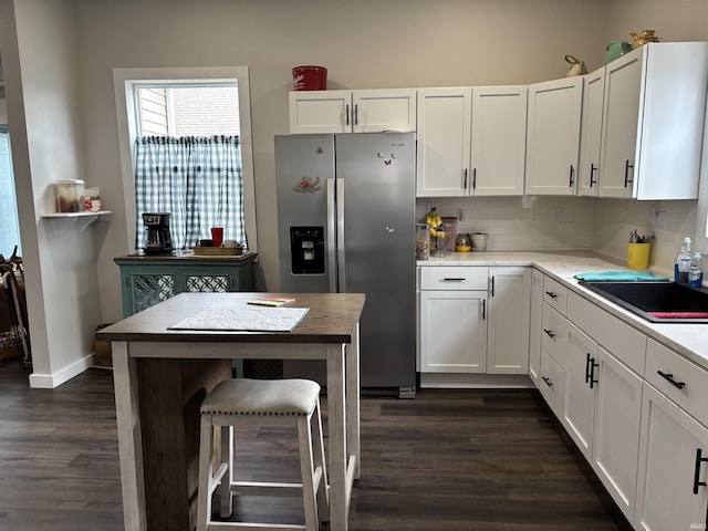 kitchen featuring tasteful backsplash, white cabinets, dark wood finished floors, stainless steel refrigerator with ice dispenser, and a sink