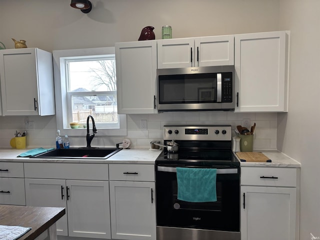 kitchen with stainless steel appliances, a sink, white cabinets, and decorative backsplash