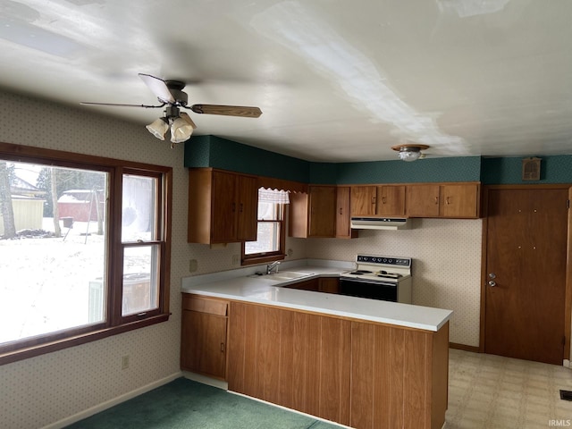 kitchen with brown cabinets, light floors, white range with electric cooktop, under cabinet range hood, and wallpapered walls