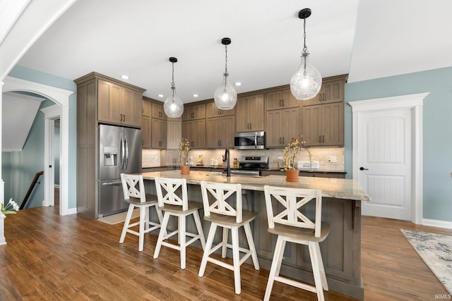 kitchen with arched walkways, decorative backsplash, dark wood-type flooring, decorative light fixtures, and stainless steel appliances