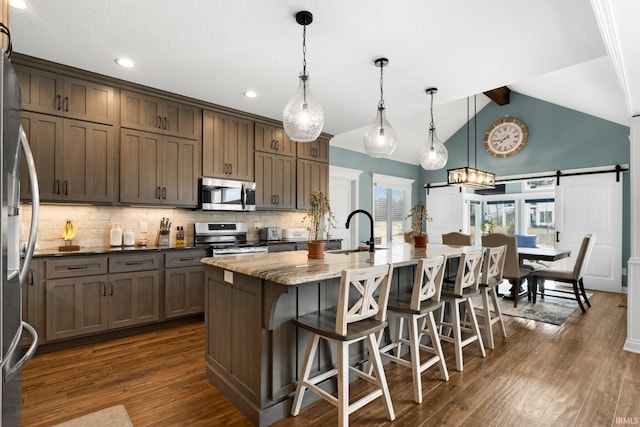 kitchen with a barn door, dark wood finished floors, a sink, stainless steel appliances, and backsplash