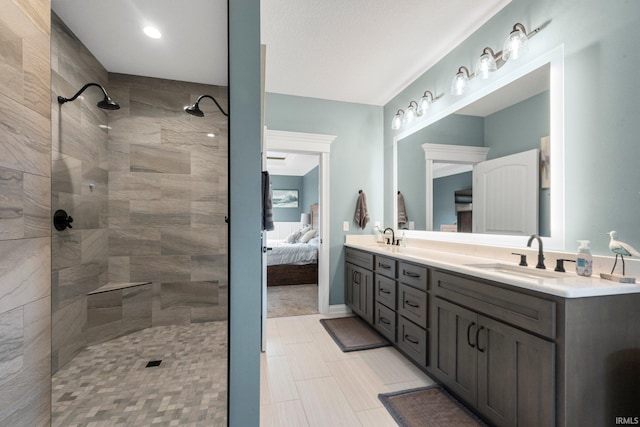 bathroom with double vanity, connected bathroom, a tile shower, and a sink