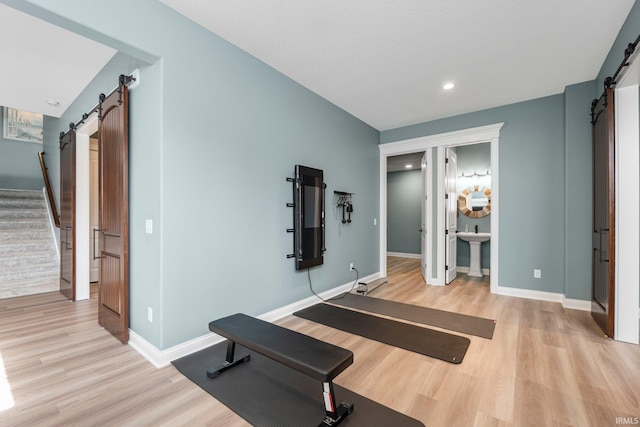 workout area featuring light wood finished floors, a barn door, recessed lighting, and baseboards