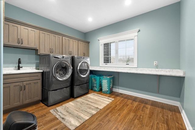 clothes washing area featuring cabinet space, a sink, wood finished floors, washer and dryer, and baseboards