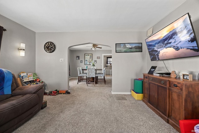 carpeted living area with baseboards, arched walkways, and a ceiling fan