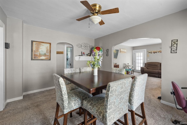 carpeted dining space with arched walkways, a ceiling fan, and baseboards