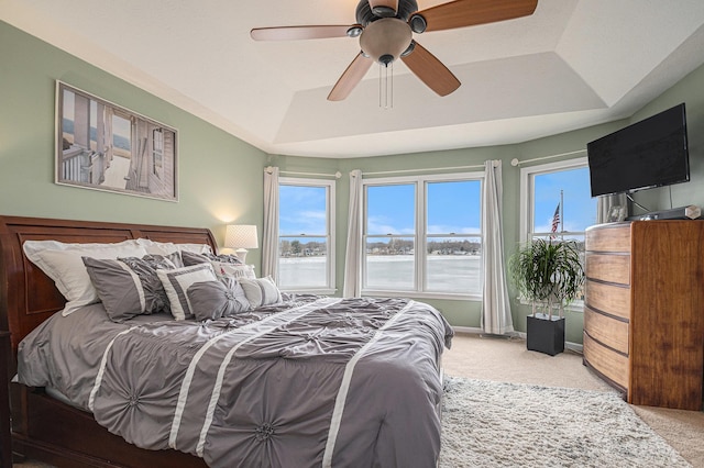 carpeted bedroom with multiple windows, a raised ceiling, a ceiling fan, and baseboards