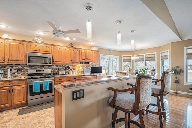 kitchen with stainless steel appliances, decorative light fixtures, a kitchen bar, and tasteful backsplash