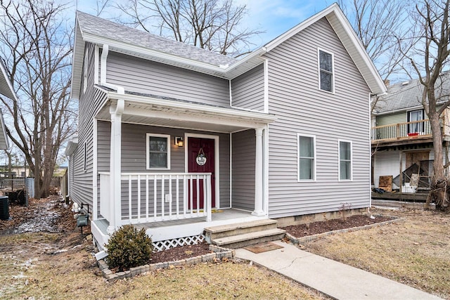 traditional-style house with a porch, roof with shingles, and central AC unit