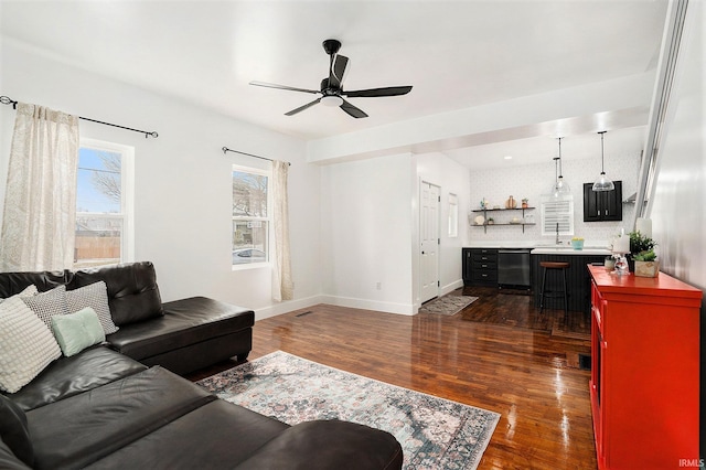 living room with a ceiling fan, visible vents, baseboards, and dark wood-style flooring