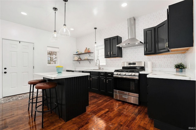 kitchen featuring light countertops, a sink, gas range, dark cabinetry, and wall chimney exhaust hood