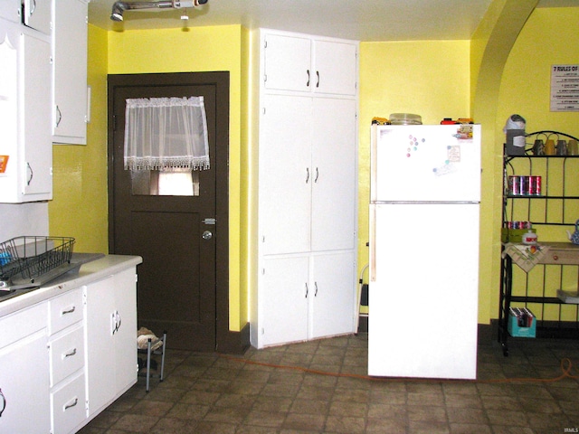 kitchen with light countertops, freestanding refrigerator, white cabinets, and arched walkways