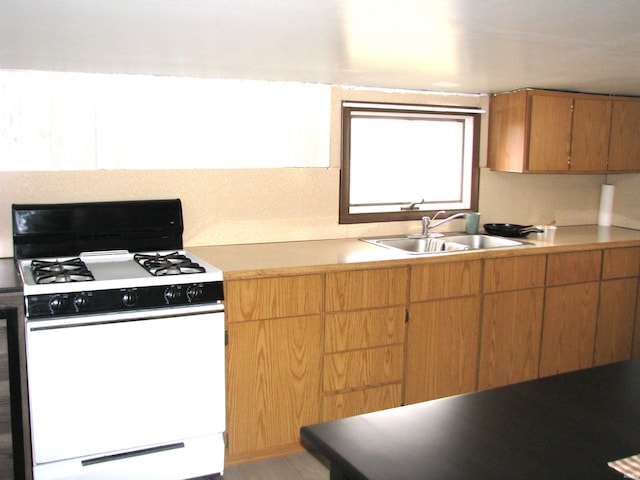 kitchen with brown cabinetry, light countertops, a sink, and white gas stove