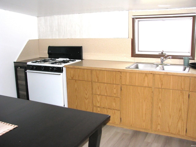 kitchen featuring white gas stove, light wood-style flooring, a sink, light countertops, and light brown cabinetry