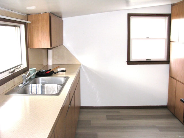 kitchen featuring light countertops, a sink, baseboards, and wood finished floors