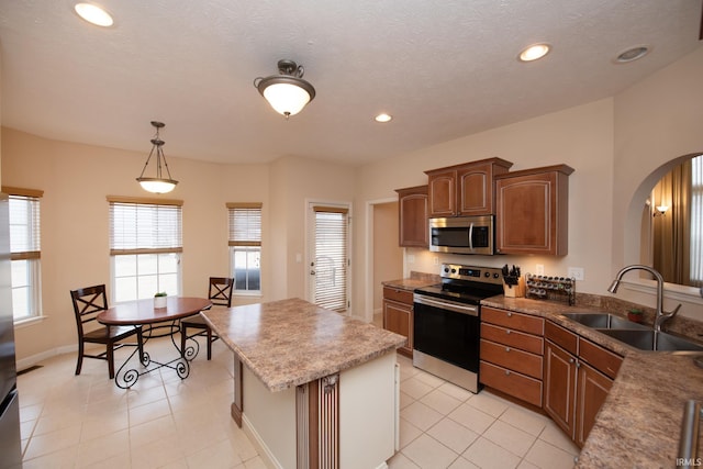 kitchen with arched walkways, pendant lighting, appliances with stainless steel finishes, a sink, and a kitchen island