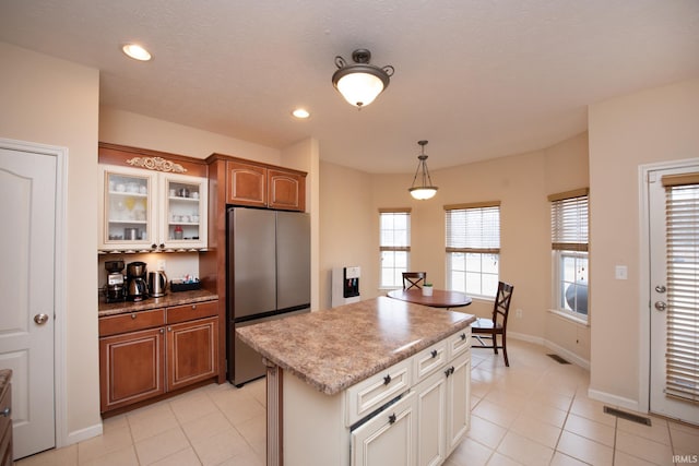 kitchen featuring glass insert cabinets, visible vents, freestanding refrigerator, a center island, and decorative light fixtures