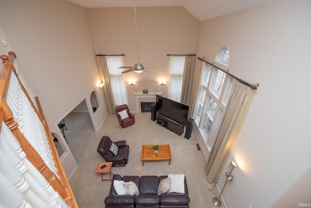 living area with ceiling fan, high vaulted ceiling, carpet flooring, and a glass covered fireplace