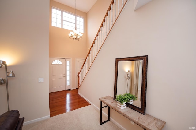 foyer with carpet floors, a high ceiling, a chandelier, baseboards, and stairs