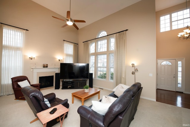 carpeted living room with high vaulted ceiling, baseboards, a fireplace with flush hearth, and ceiling fan with notable chandelier