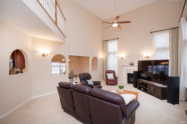 living area with light carpet, baseboards, a ceiling fan, a glass covered fireplace, and high vaulted ceiling