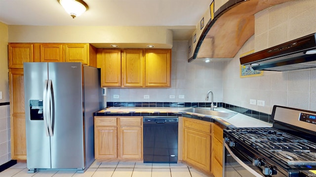 kitchen featuring tile countertops, under cabinet range hood, stainless steel appliances, a sink, and backsplash