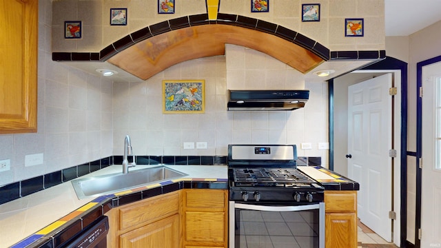 kitchen with tile countertops, tasteful backsplash, a sink, gas range, and extractor fan