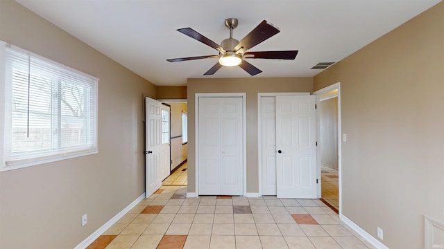 unfurnished bedroom featuring light tile patterned floors, baseboards, visible vents, ceiling fan, and two closets