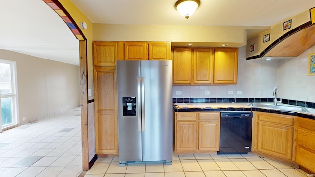 kitchen with a sink, black dishwasher, tile counters, tasteful backsplash, and stainless steel fridge