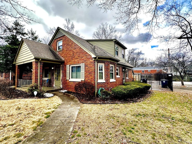 view of side of property featuring a yard, covered porch, brick siding, and fence